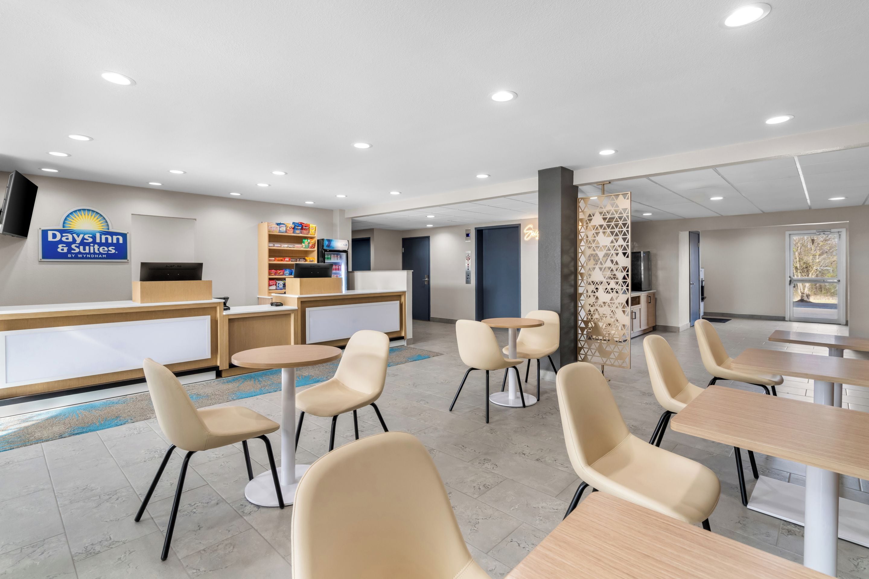 A hotel reception area with a reception desk, a refrigerator, a vending machine, and a seating area with chairs and tables.