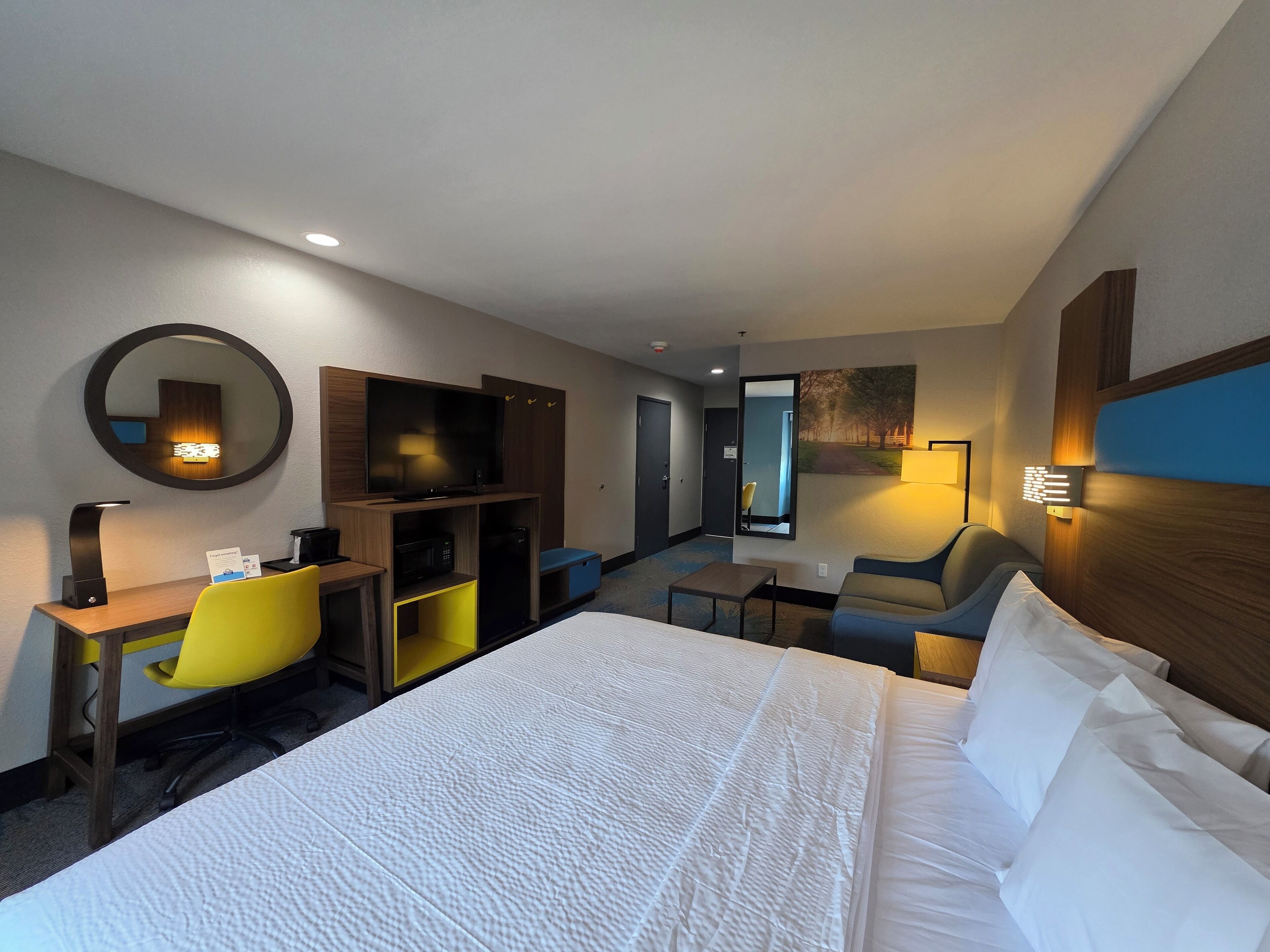 A hotel room with a large bed, a desk with a chair, a television, and a small table.