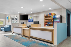 A reception area with a sign for Days Inn & Suites, a refrigerator stocked with snacks, a television, and a blue chair. - Days Inn & Suites by Wyndham Brandon Amphitheater (Brandon)