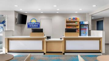 A reception area with a sign for Days Inn & Suites, a self-service kiosk, a snack shelf, and a refrigerator with beverages.