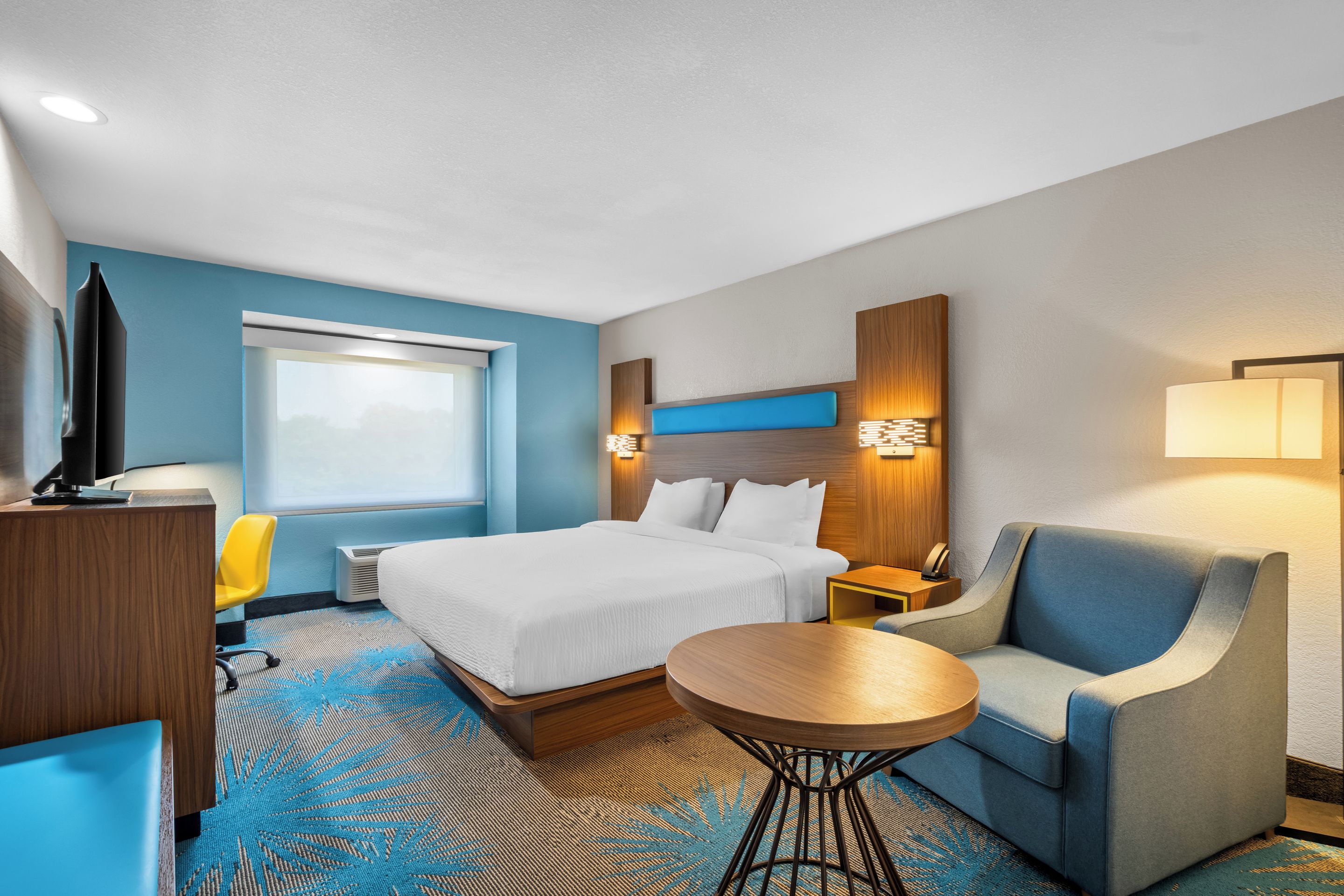 A hotel room with a bed, a desk, a chair, a round table, and a TV.