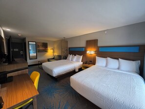 Ein Hotelzimmer mit zwei Betten, einem Schreibtisch, einem Stuhl und einem Fernseher.