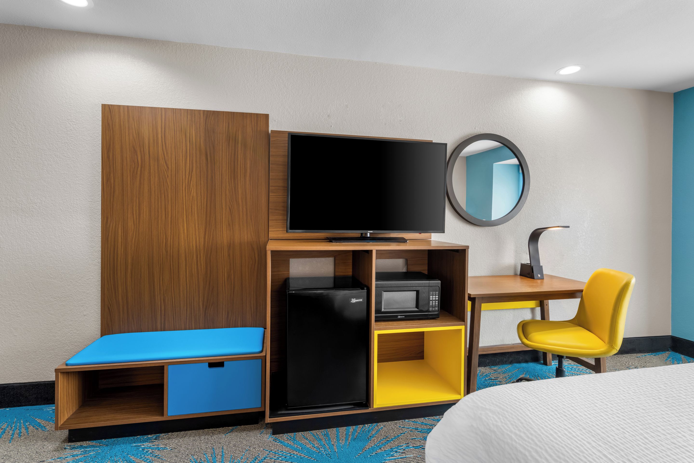 A hotel room with a bed, a desk with a chair, a television, a refrigerator, and a microwave.