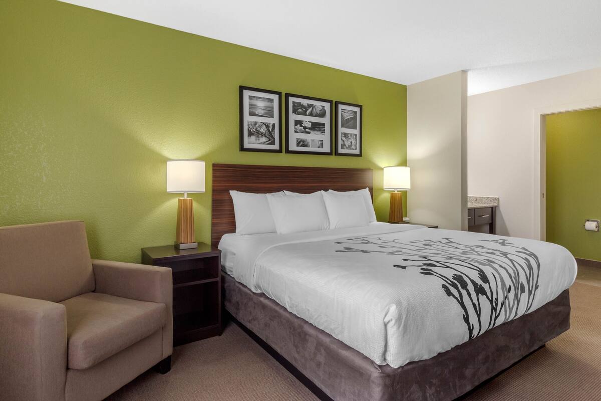 A hotel room with a bed, a chair, two bedside tables with lamps, and three framed pictures on the wall.