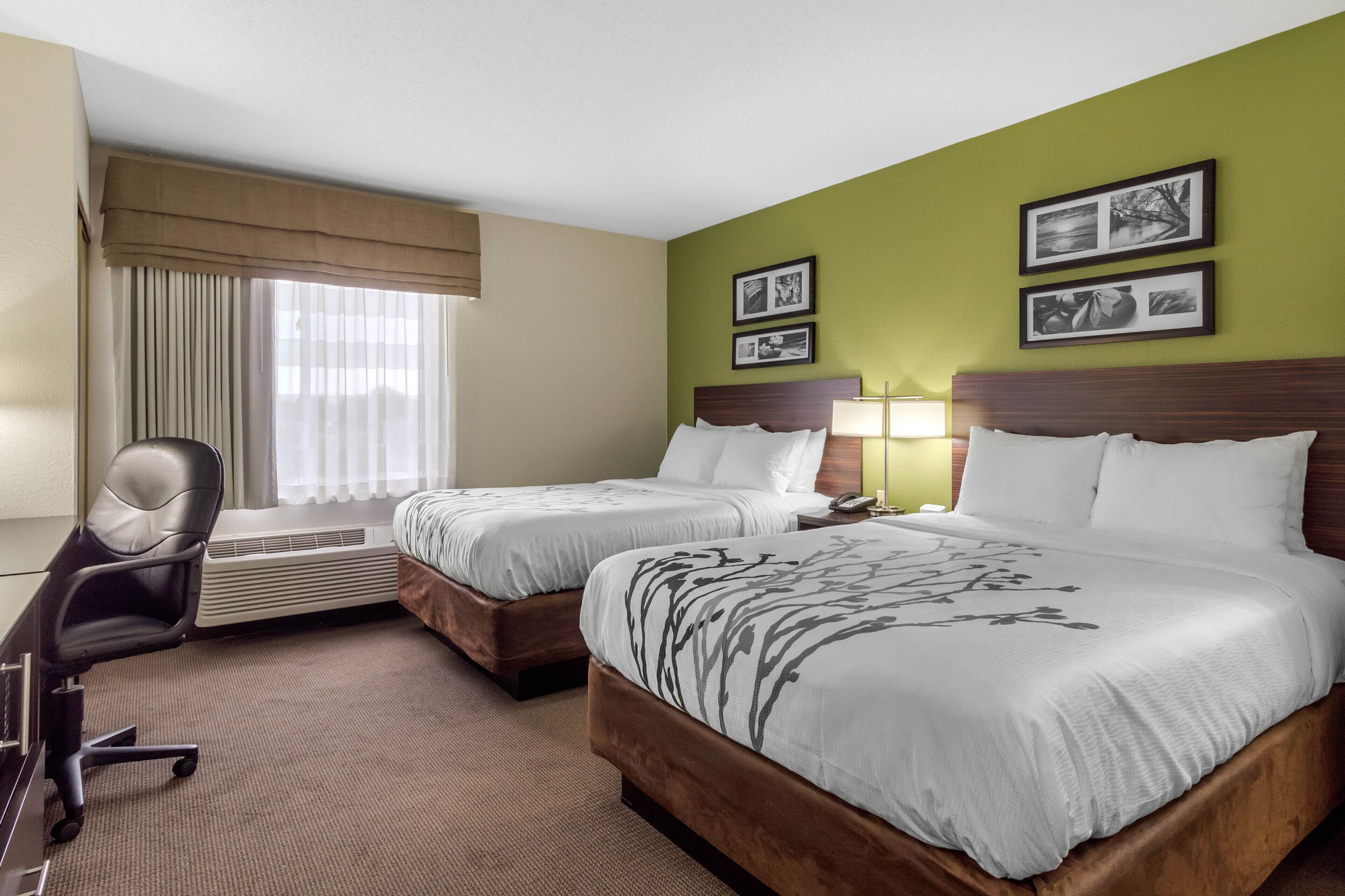 A hotel room with two beds, a desk, and a chair. There are two framed pictures on the wall.