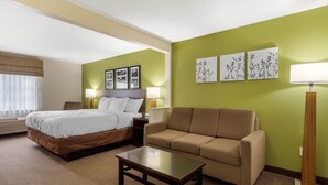Una habitación de hotel con cama, sofá, mesa de centro y dos lámparas de pared.
