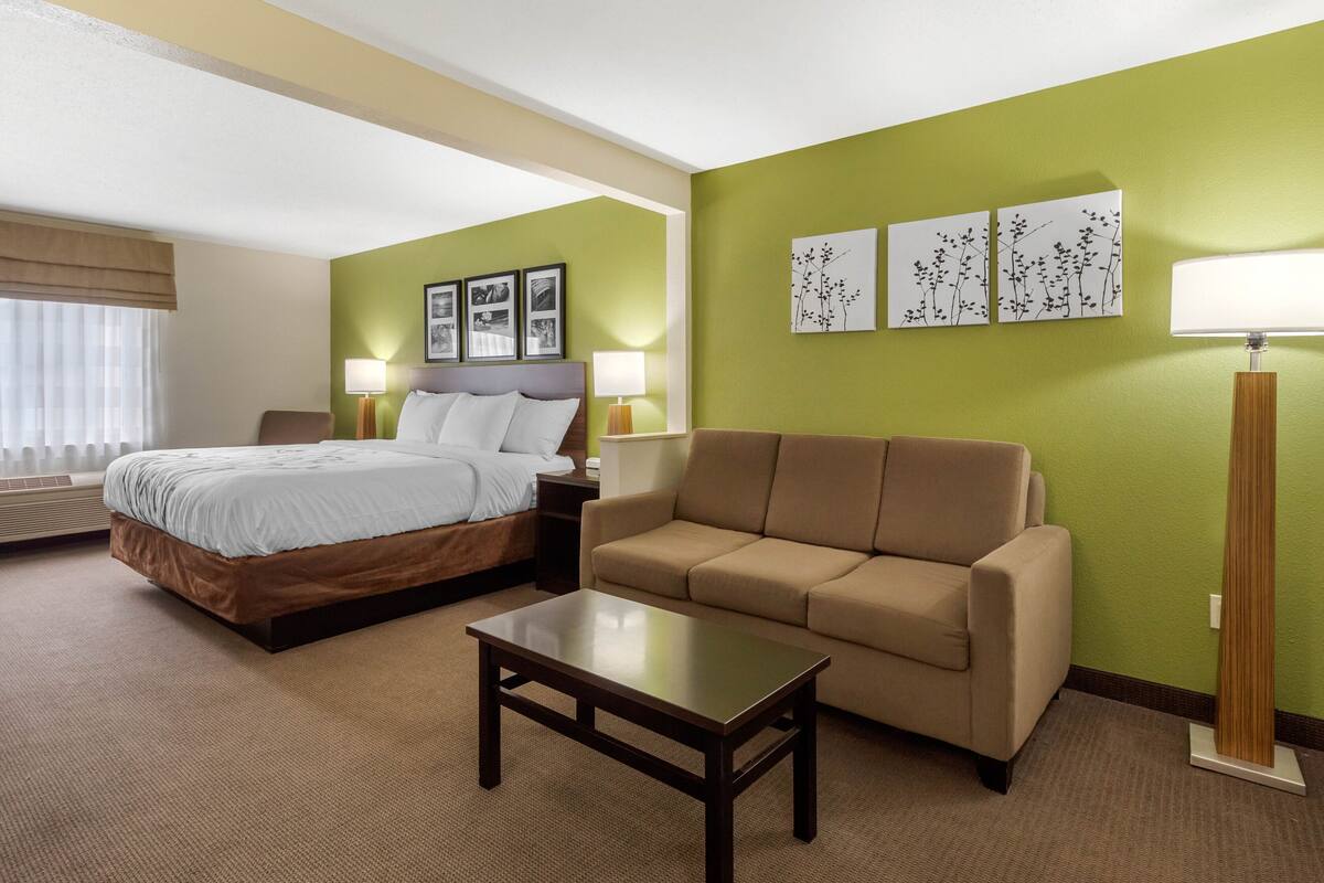 A hotel room with a bed, a sofa, a coffee table, and two wall-mounted lamps.