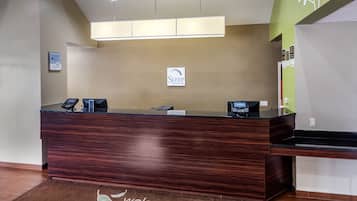 A reception desk with a sign reading "Sleep Inn & Suites," a digital phone, and a "Welcome" mat.