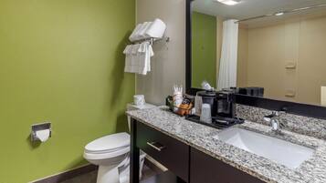 A bathroom with a green wall, white toilet, granite countertop, sink, and a mirror.