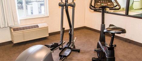 Ginásio interno com duas máquinas elípticas, uma bicicleta ergométrica e uma bola de exercícios grande.