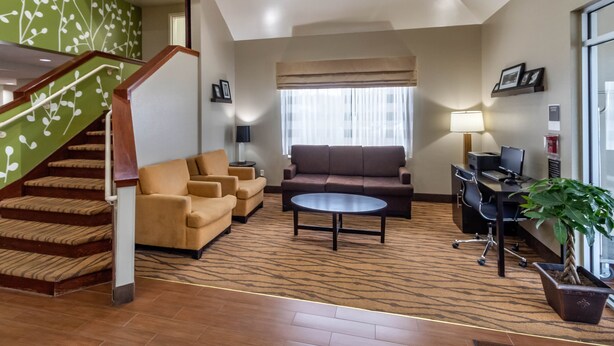 Salón de hotel con una escalera, sofás, una mesa de centro, un escritorio con una computadora y una planta en maceta.