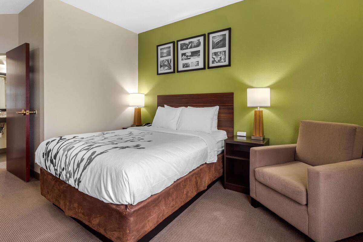 A hotel room with a large bed, two bedside lamps, a chair, and three framed pictures on the wall.