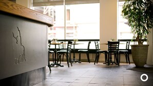 Interior de restaurante com balcão de madeira, chão de azulejos e cadeiras pretas.