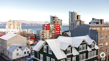Paesaggio costiero con edifici moderni e tradizionali, vista sul mare e montagne sullo sfondo.