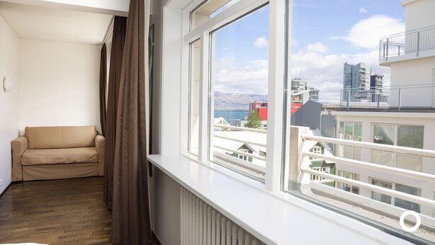 Quarto com janela e vista para a cidade, sofá bege e radiador.