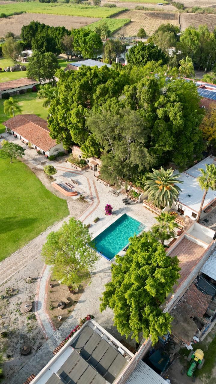 An aerial view of a property with a swimming pool, surrounded by lush greenery and a few buildings.