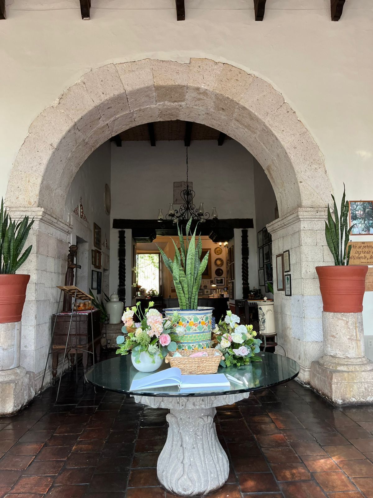 Una mesa con un libro, flores, un arco y plantas en macetas.