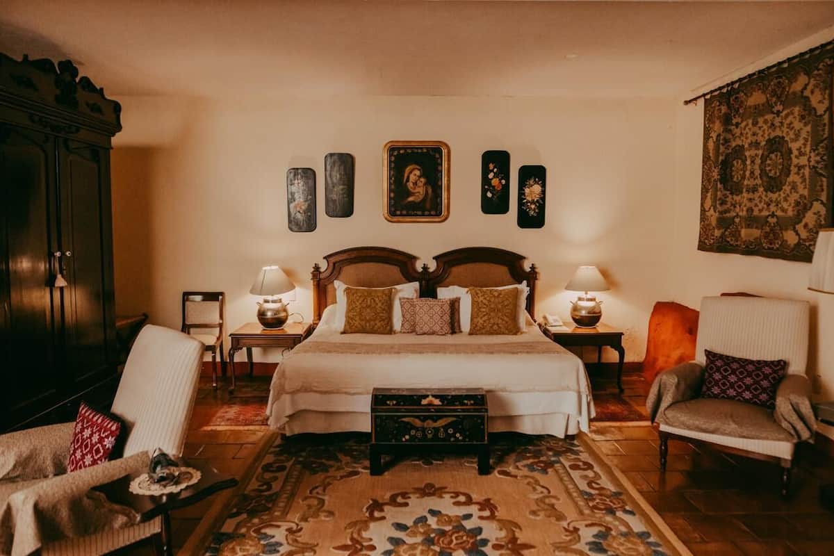 A traditional bedroom with a large bed, two bedside tables, a chest of drawers, and a patterned rug.