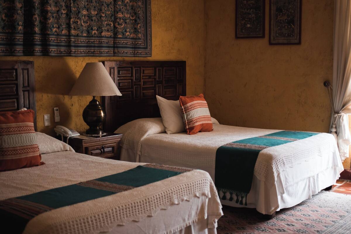 A room with two beds, a nightstand with a lamp, a telephone, and a wall with framed pictures.