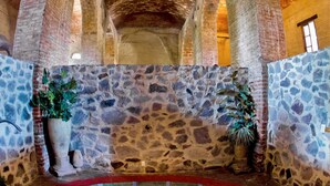 A stone-walled indoor pool with a red border, surrounded by arches and potted plants.
