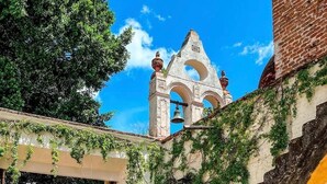 A courtyard with a stone staircase, a bell tower, and a covered walkway with ivy.