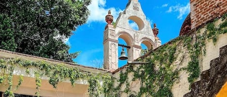 A courtyard with a stone staircase, a bell tower, and a covered walkway with ivy.