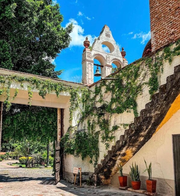A courtyard with a stone staircase, a bell tower, and a covered walkway with ivy.
