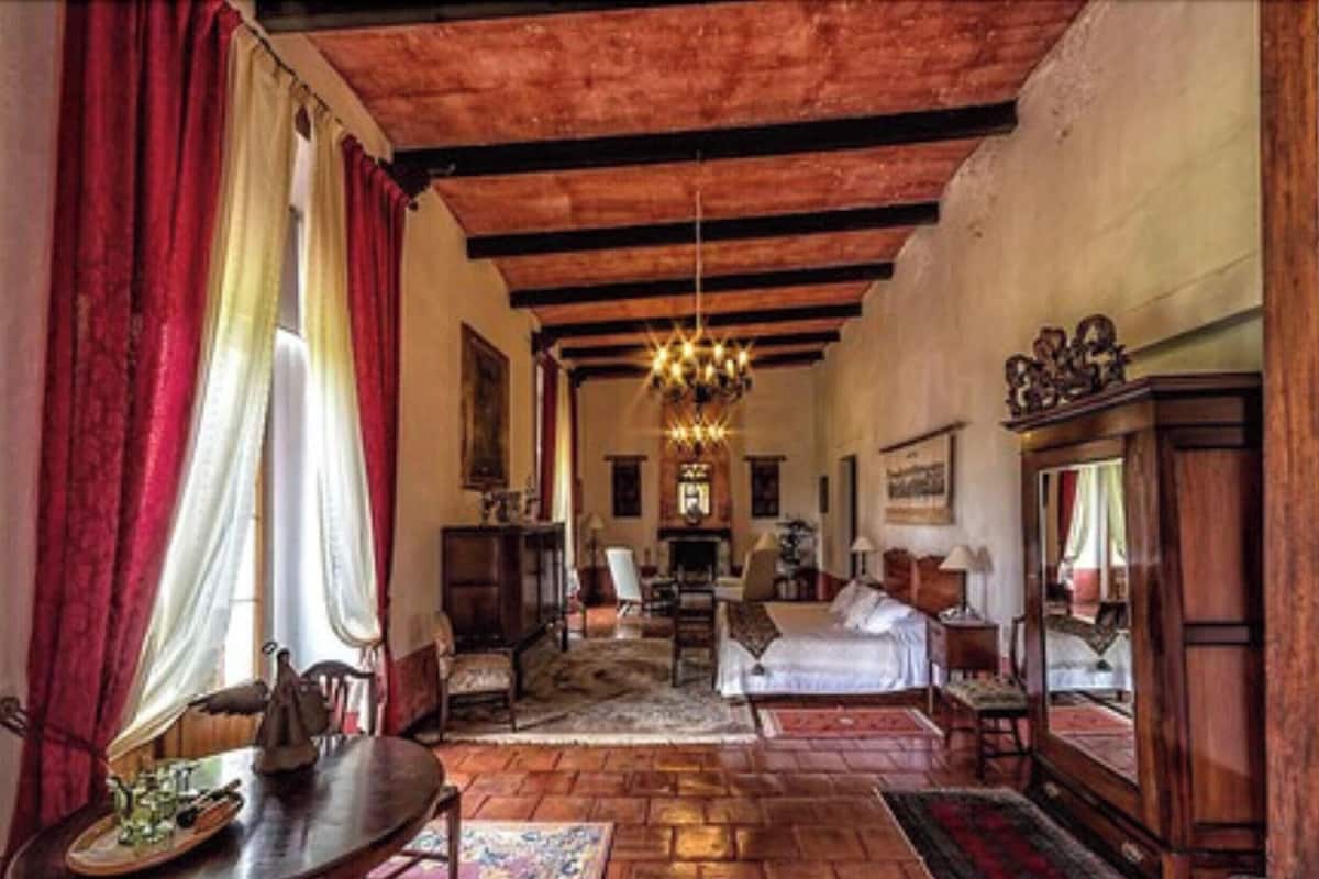 A spacious living room with a fireplace, wooden beams, and a chandelier.
