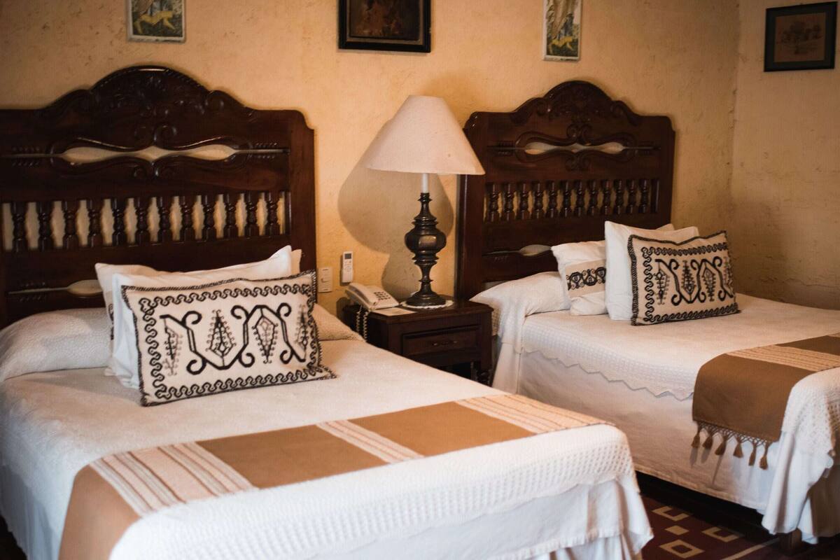 Two twin beds with headboards, a bedside table with a lamp, and a patterned pillow.