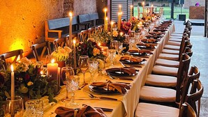 A long dining table set for a meal in a rustic brick-walled room with hanging lanterns.