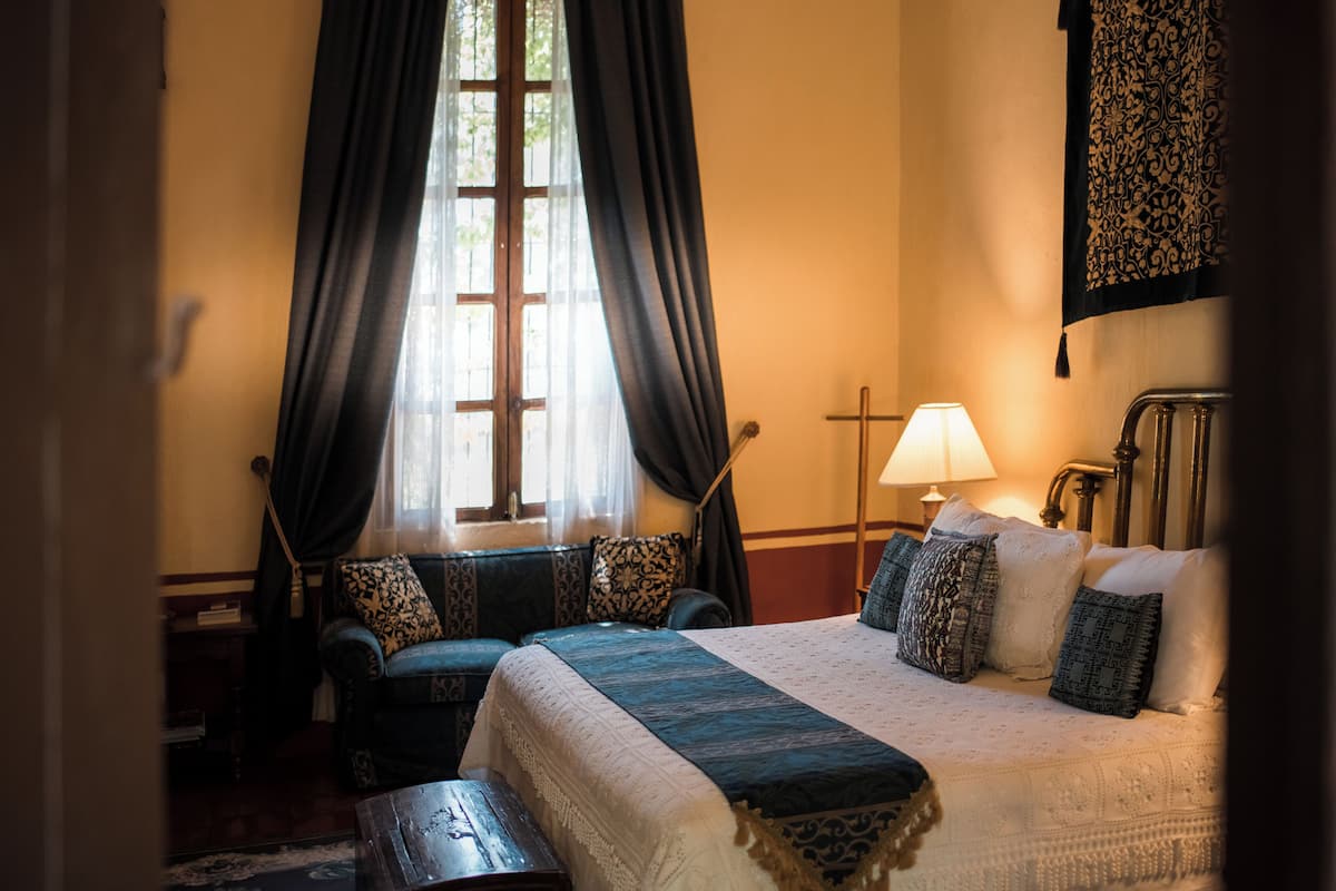 A hotel room with a large bed, a sofa, a nightstand, and a lamp.