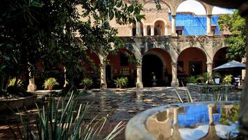 Un patio con una fuente, plantas en macetas y un edificio con arcos.