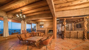 Una stanza spaziosa con soffitto in legno, un grande tavolo da pranzo e sedie. È presente un camino e un angolo bar con un design in legno originale.