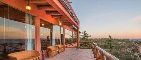 Una terraza con banca de madera, pared de vidrio y vistas al paisaje.