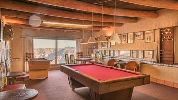 Una mesa de billar en una sala con vigas de madera, cuadros en la pared y vistas a las montañas.