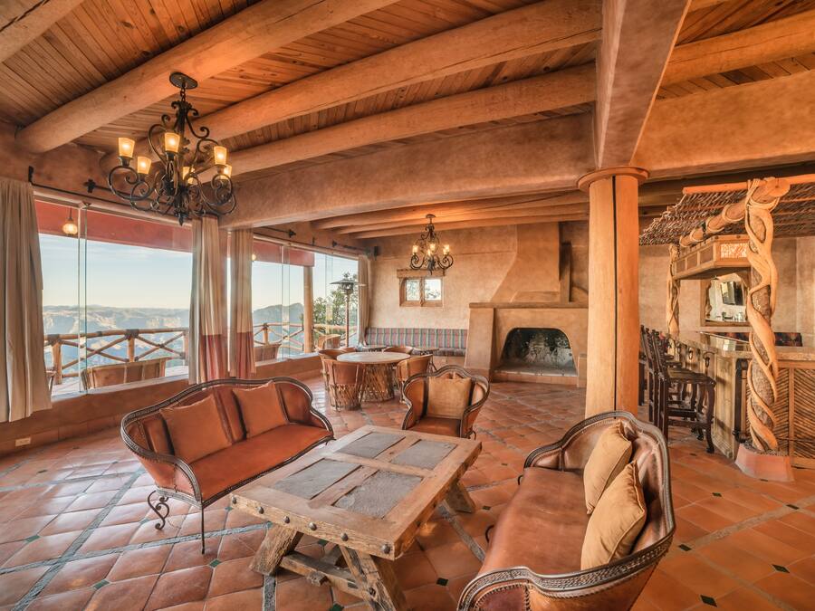 A rustic interior with a wooden ceiling, large windows, a fireplace, and a bar area.