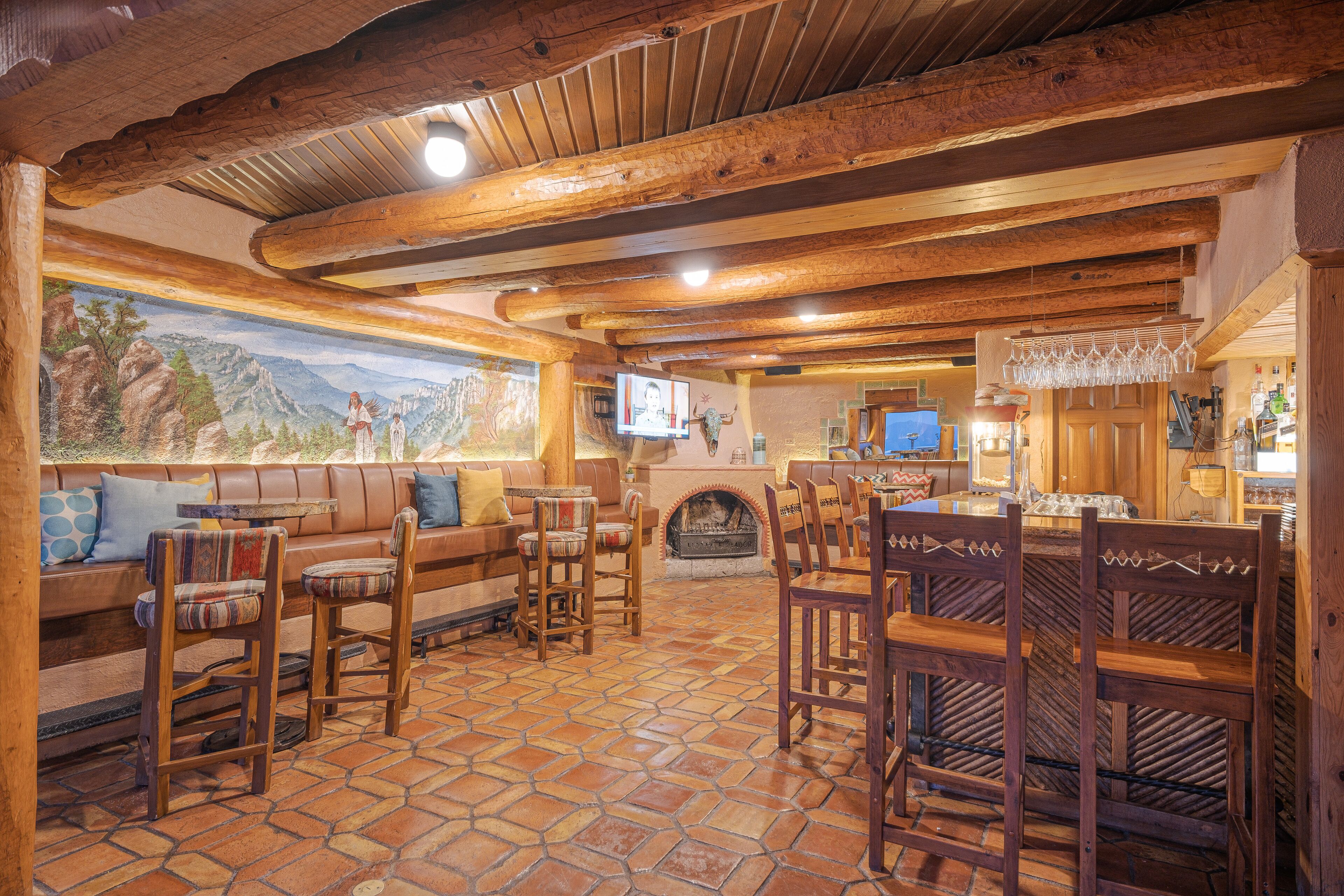 A cozy interior with a stone-tiled floor, wooden furniture, a fireplace, and a mural on the wall.