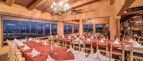A restaurant with multiple tables set for dining, large windows offering a view, and a wooden ceiling.