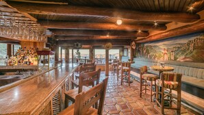 Zona bar rustica con mobili in legno, pavimento in pietra e un affresco al muro.