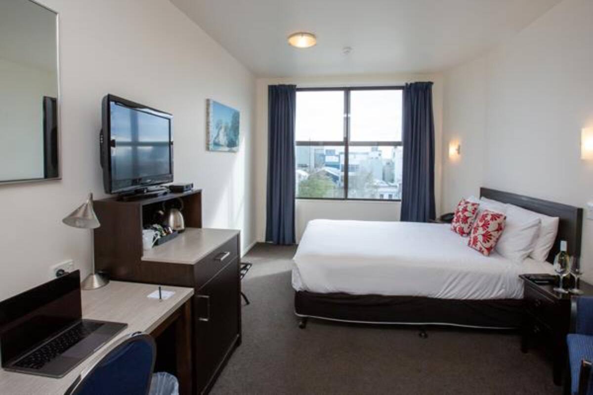 Ein Hotelzimmer mit Bett, Schreibtisch, Laptop, Fernseher und einem Fenster mit Vorhängen.