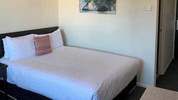 A neatly made bed with white bedding and a single red and white striped pillow. A painting of a coastal scene hangs above the bed.