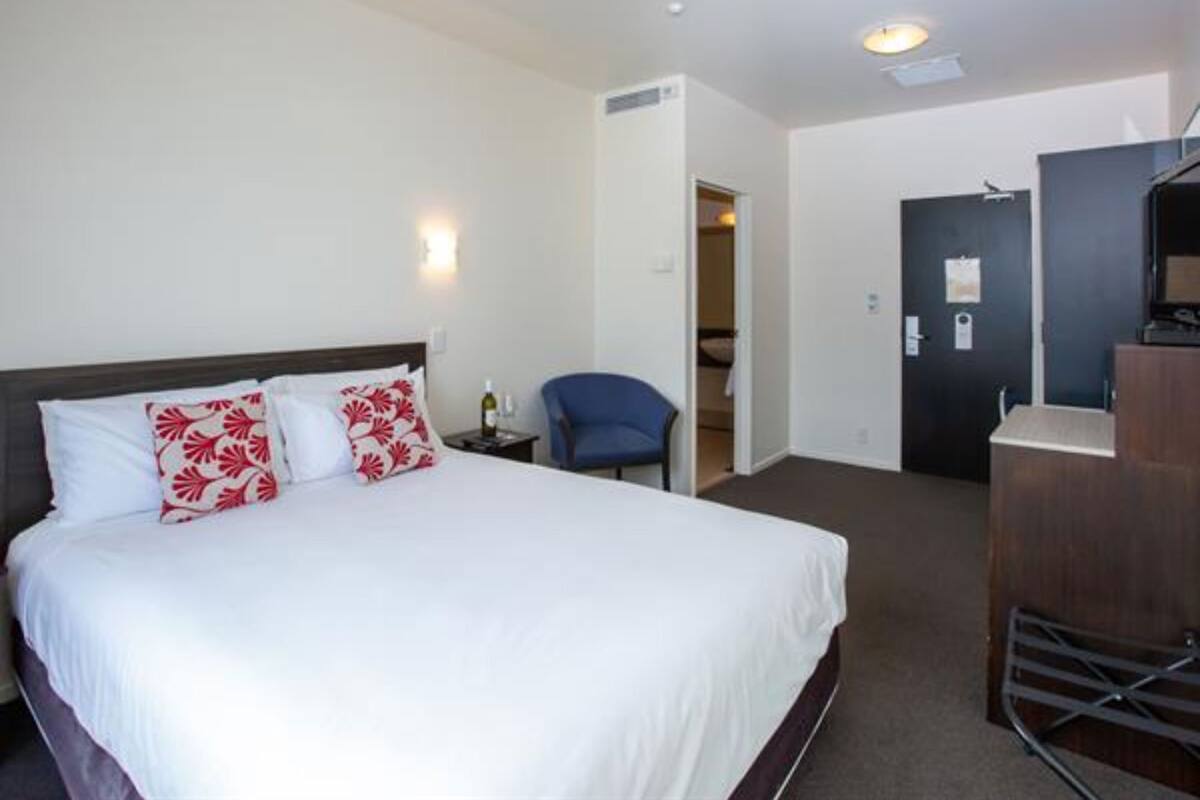 A hotel room with a bed, a chair, a desk, and a door.