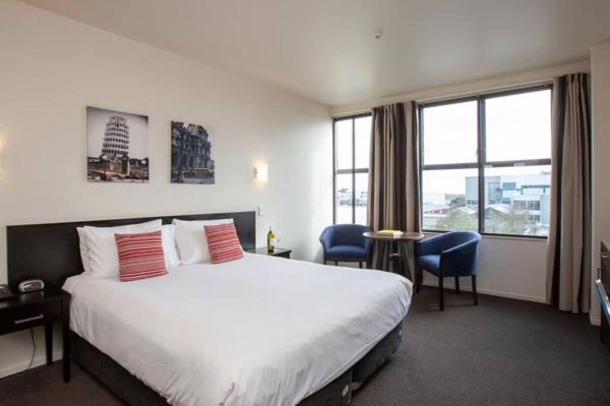 A hotel room with a large bed, two chairs, a small table, and a window with curtains.