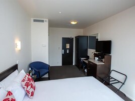 Habitación de hotel con una cama, un escritorio, una silla, un televisor y un armario.