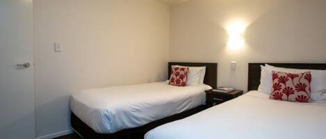A hotel room with two single beds, a nightstand, a wall-mounted light, and a door.