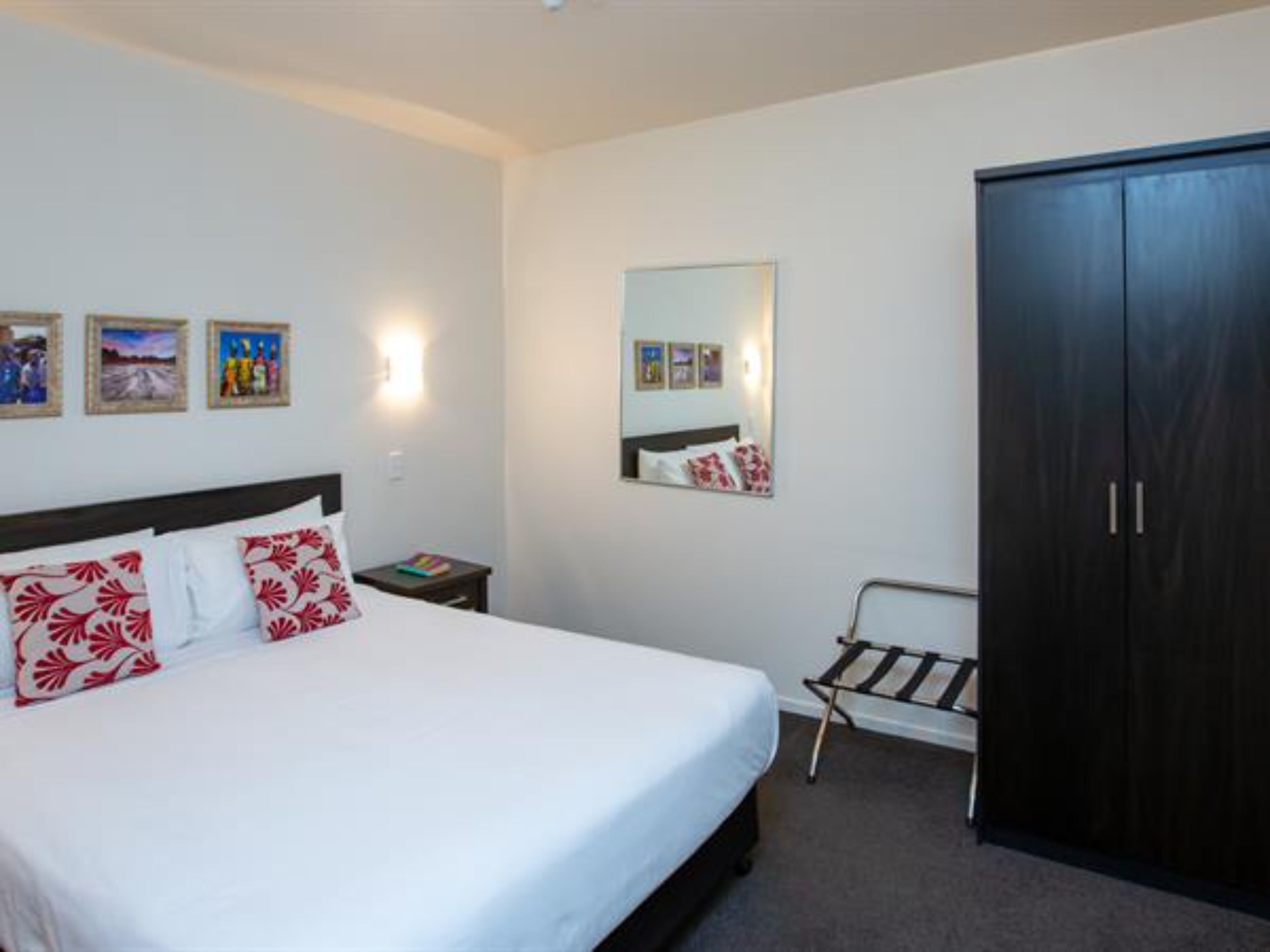 A hotel room with a bed, a nightstand, a wardrobe, and wall-mounted artwork.