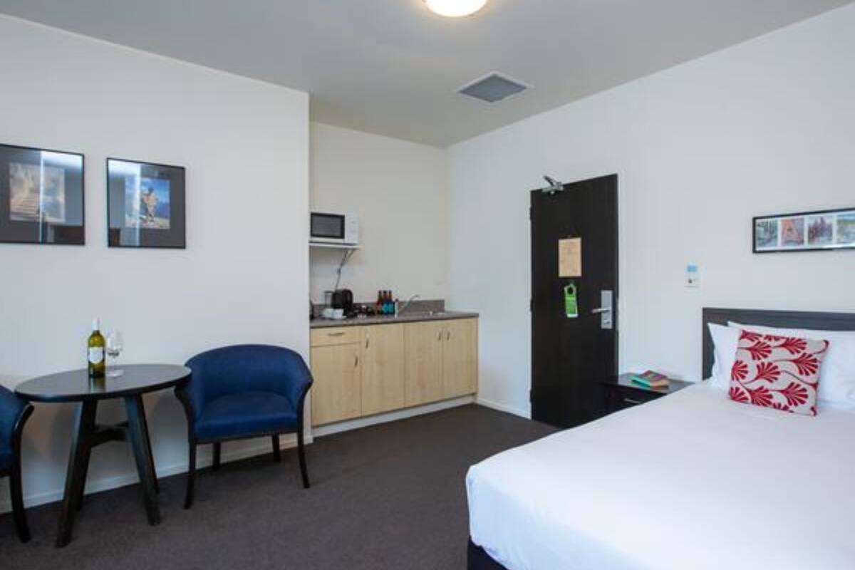 Ein Hotelzimmer mit Bett, Schreibtisch, Stuhl, einer Küchenzeile und einer Tür.