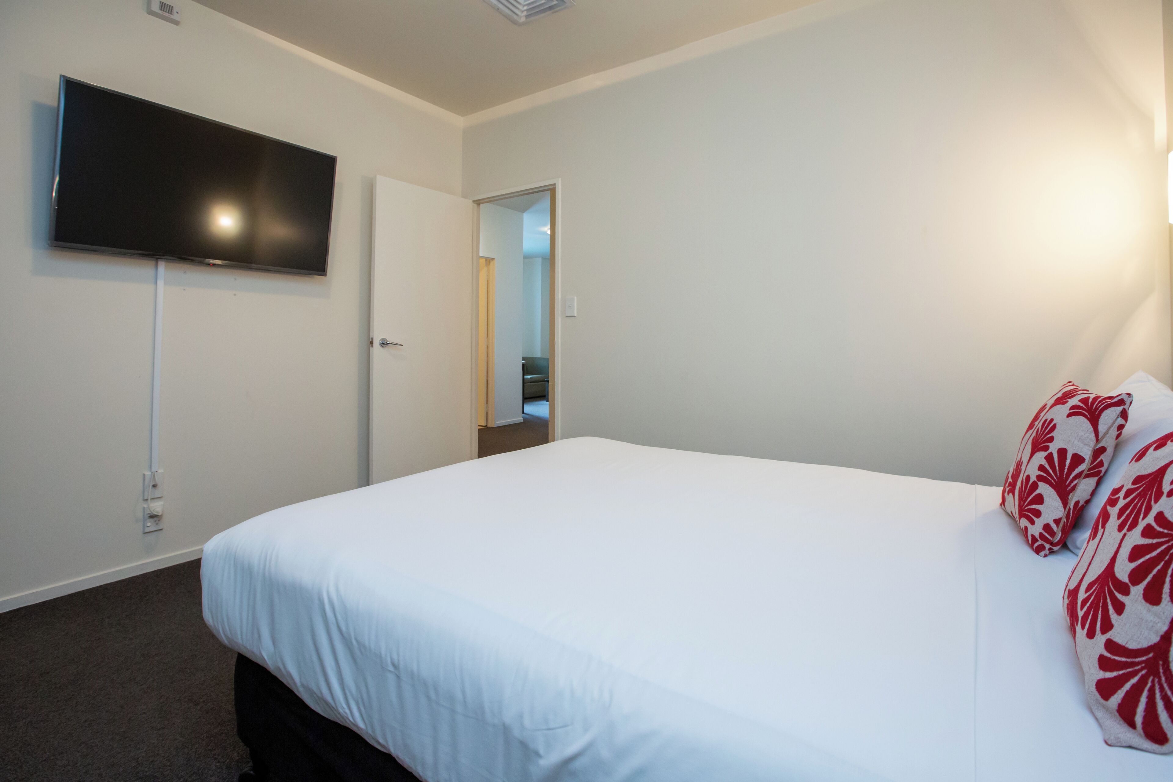 Une chambre d’hôtel avec un lit, un téléviseur à écran plat fixé au mur et une porte donnant sur un couloir.