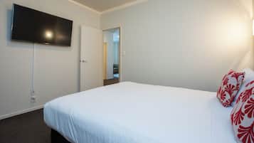 Une chambre d’hôtel avec un lit, un téléviseur à écran plat fixé au mur et une porte donnant sur un couloir.