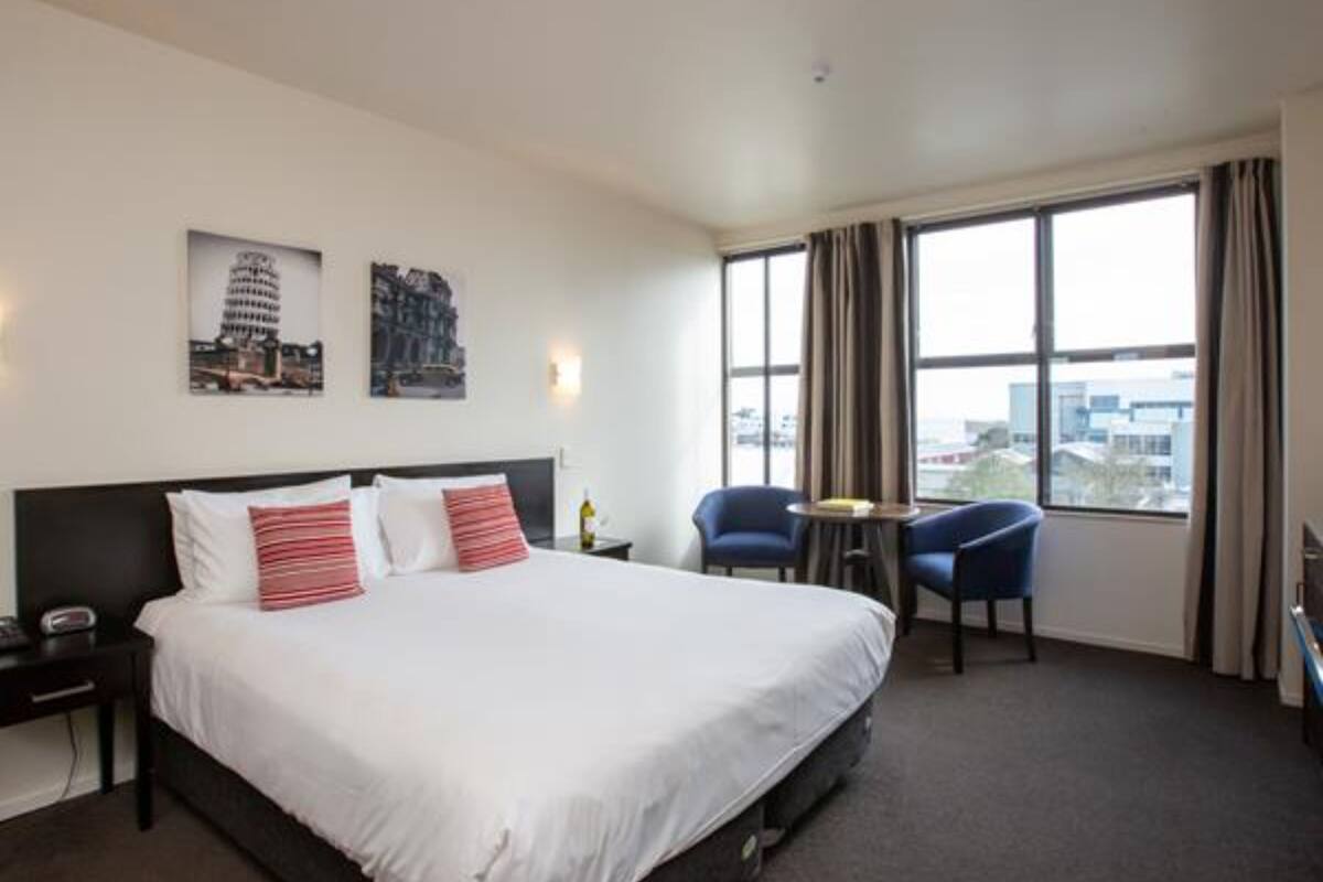 Ein Hotelzimmer mit einem großen Bett, zwei Stühlen, einem kleinen Tisch und einem Fenster mit Blick auf die Stadt.